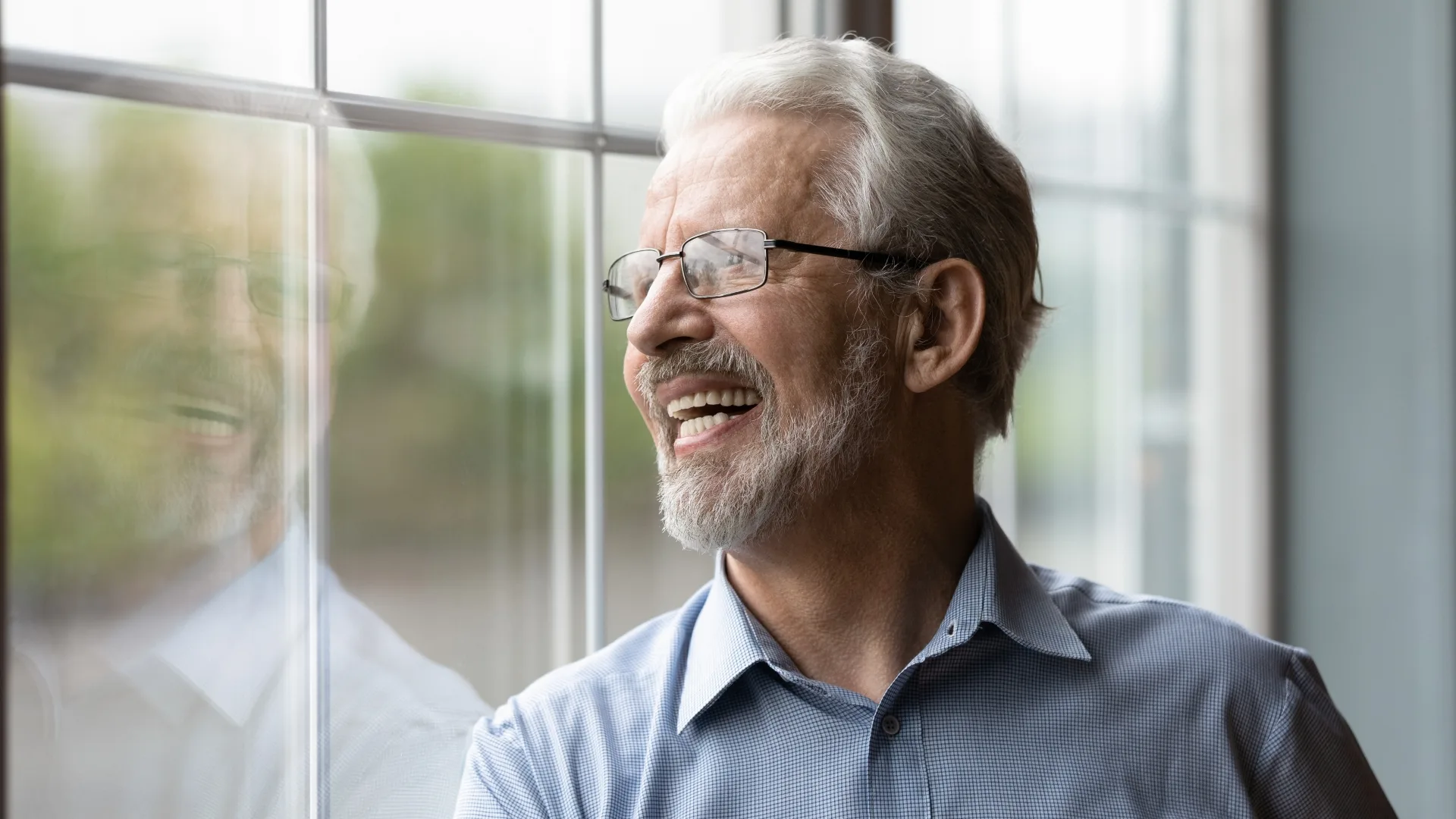 Healthy aged male stand by window laugh watch something outside