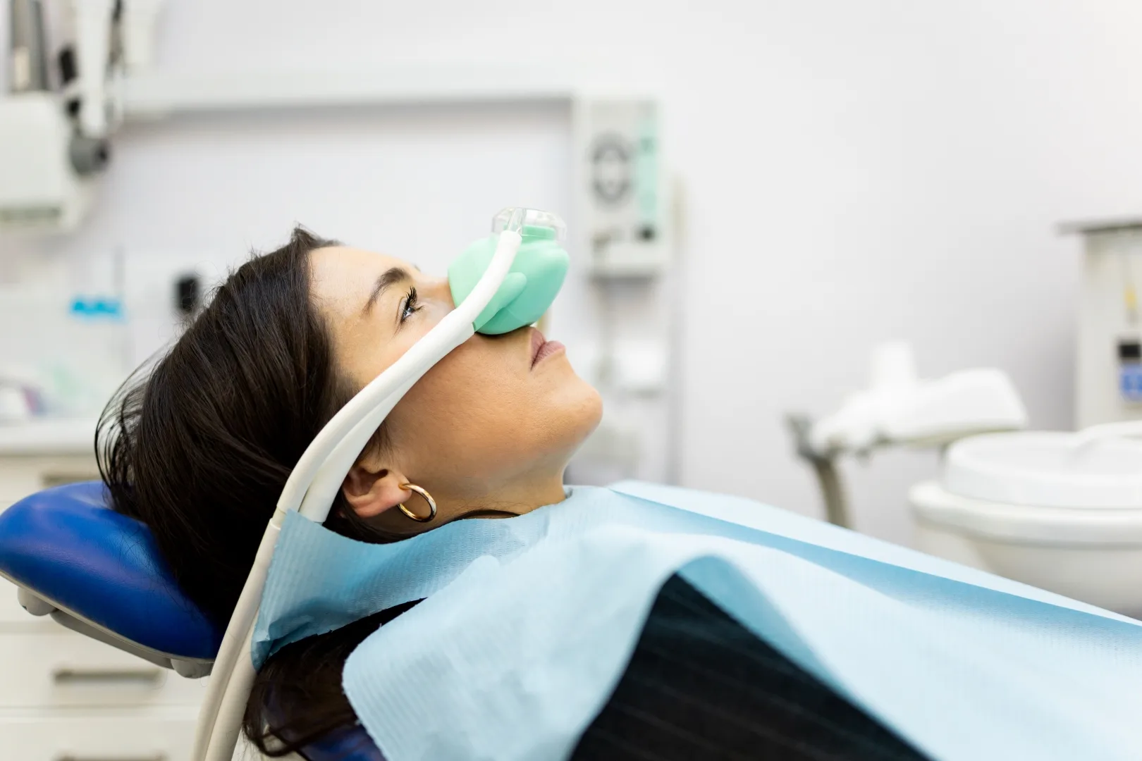 An adult woman sits in a dentist’s office wearing a nasal mask to inhale nitrous oxide. Dentist fear concept. Feeling of relaxation with laughing gas. Visit a dentist with relaxation.